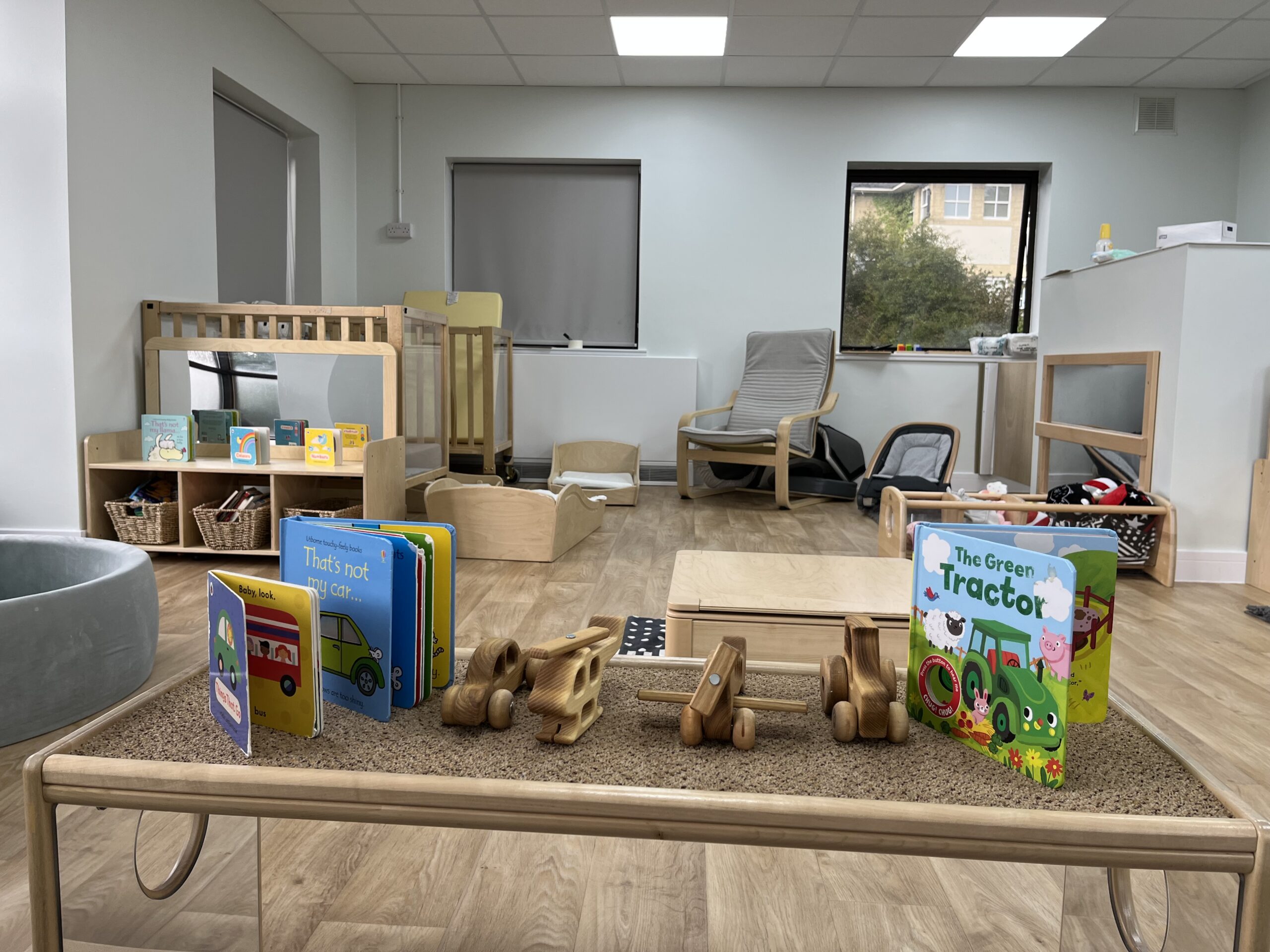 Baby room, showing cott, baby sleeping pod, rocking chair, ball pit and books on wooden cabinet.