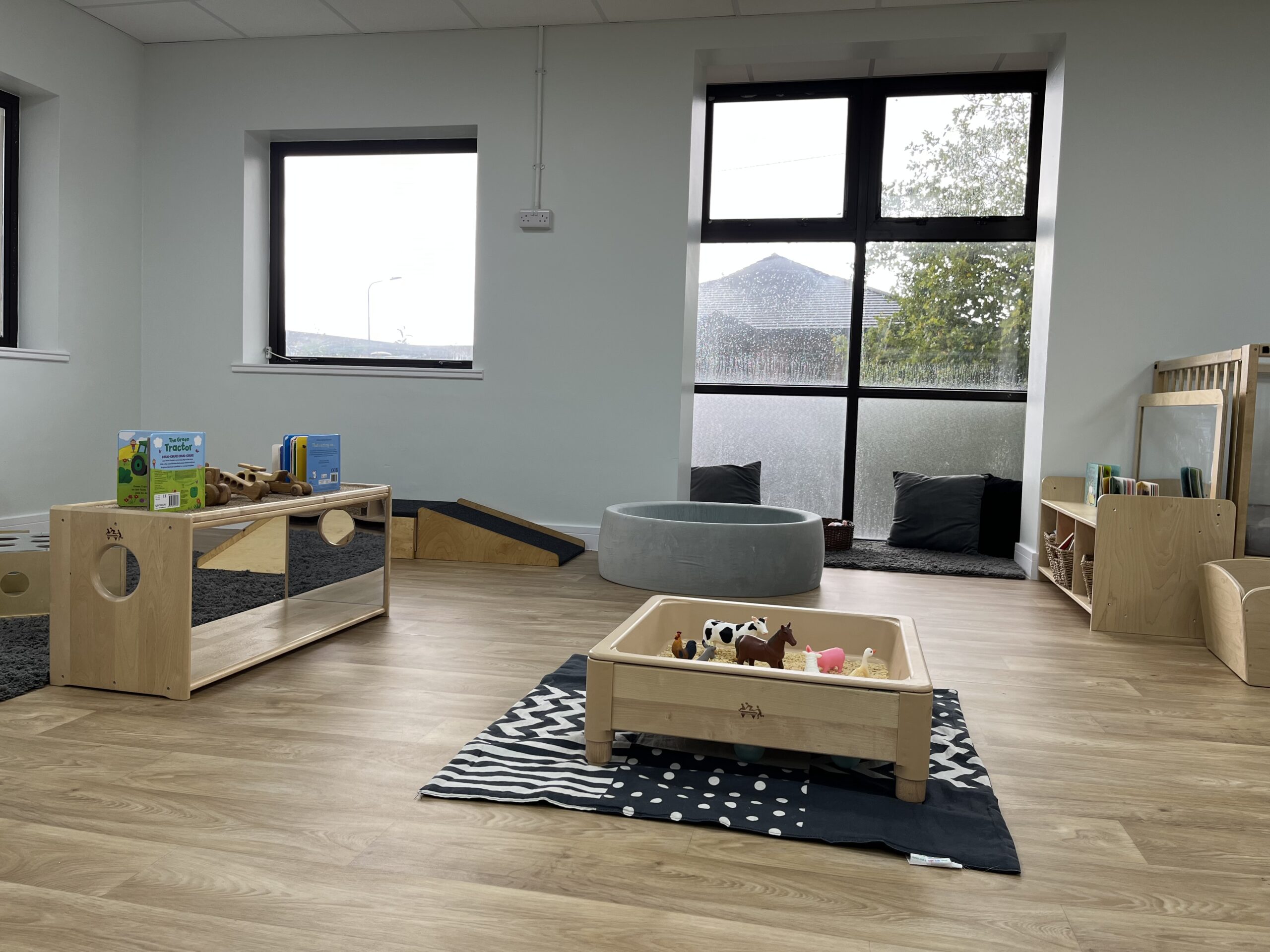Overview photo of the baby room with wooden tuff tray with farm animals in, mirrored cabinets with books and wooden toys placed on top