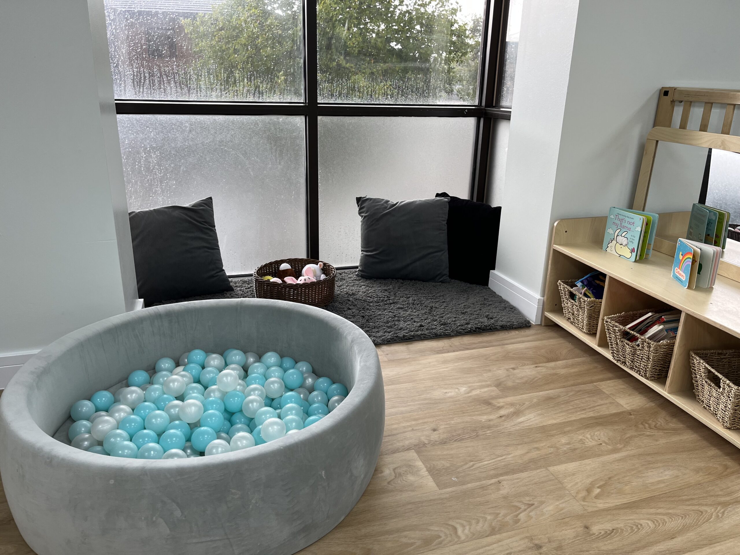 Ball pit and cosy corner with cushions and a comfy rug placed by the window with toys in a basket on the rug