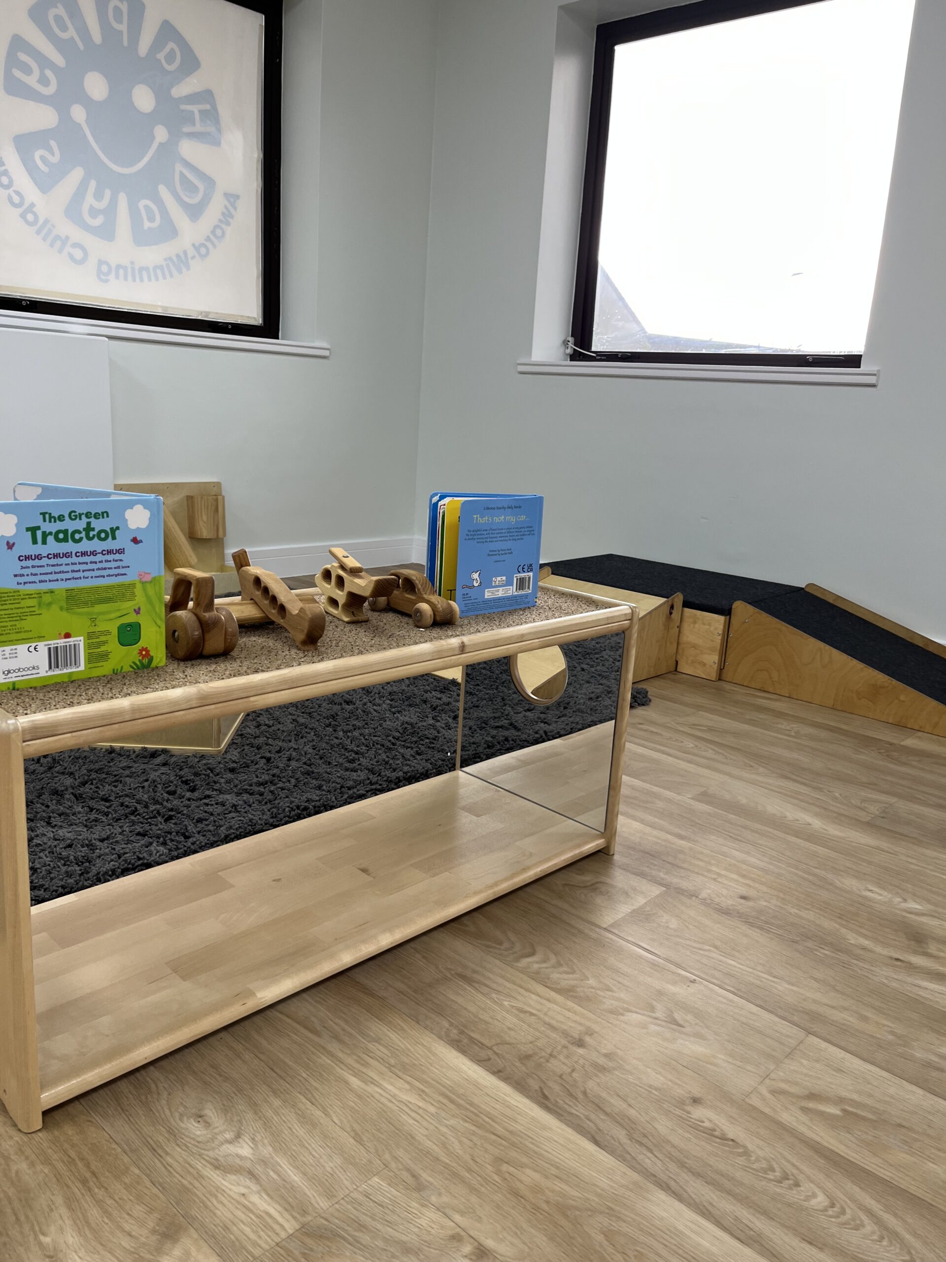 Some books and wooden cars on top of a mirrored table in the baby room.