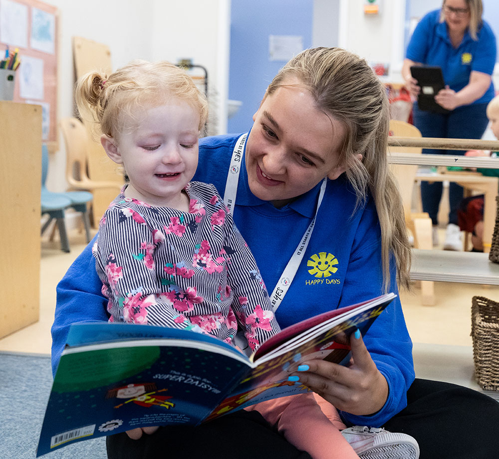 A Child at Happy Days Nurseries reading a book with a member of staff