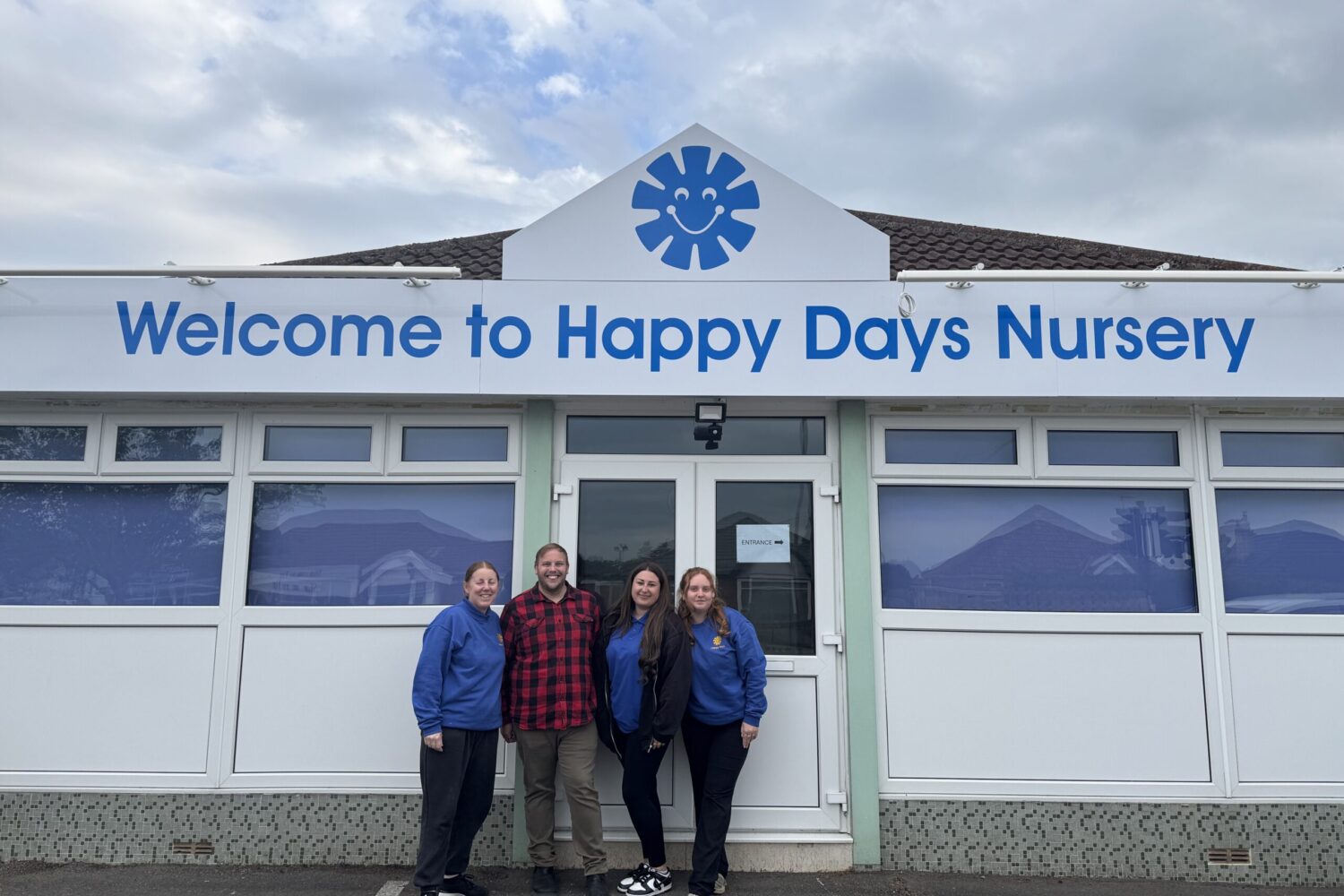 A smiley team photo with staff at Saltford stood infront of nursery with the sign in the background.