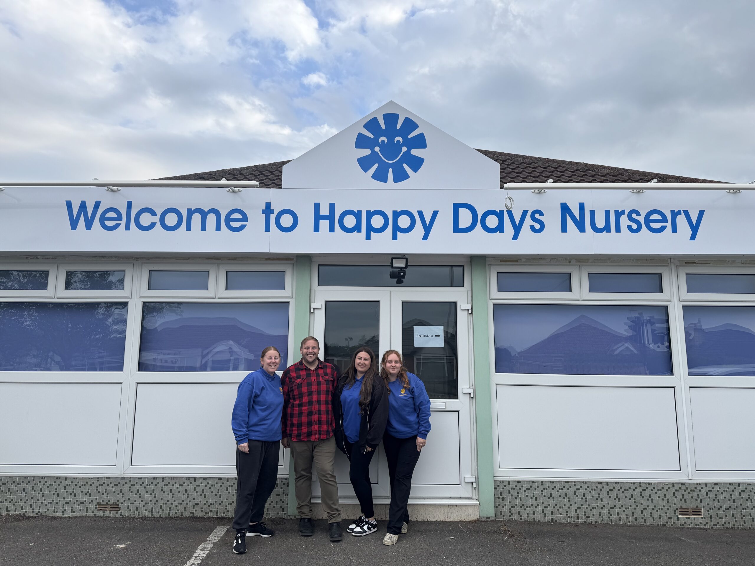 A smiley team photo with staff at Saltford stood infront of nursery with the sign in the background.