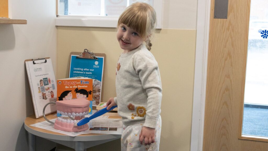 Girl learning about children's good oral health by practicing with a giant toothbrush and toy mouth.
