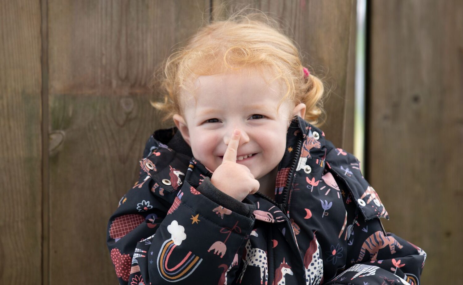 A child cheekily sat with her finger on her nose